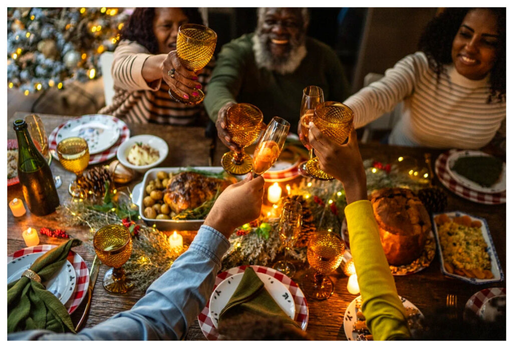 Family and friends toasting at a festive holiday dinner table with candles, golden glassware, and traditional dishes, creating a warm and joyful atmosphere