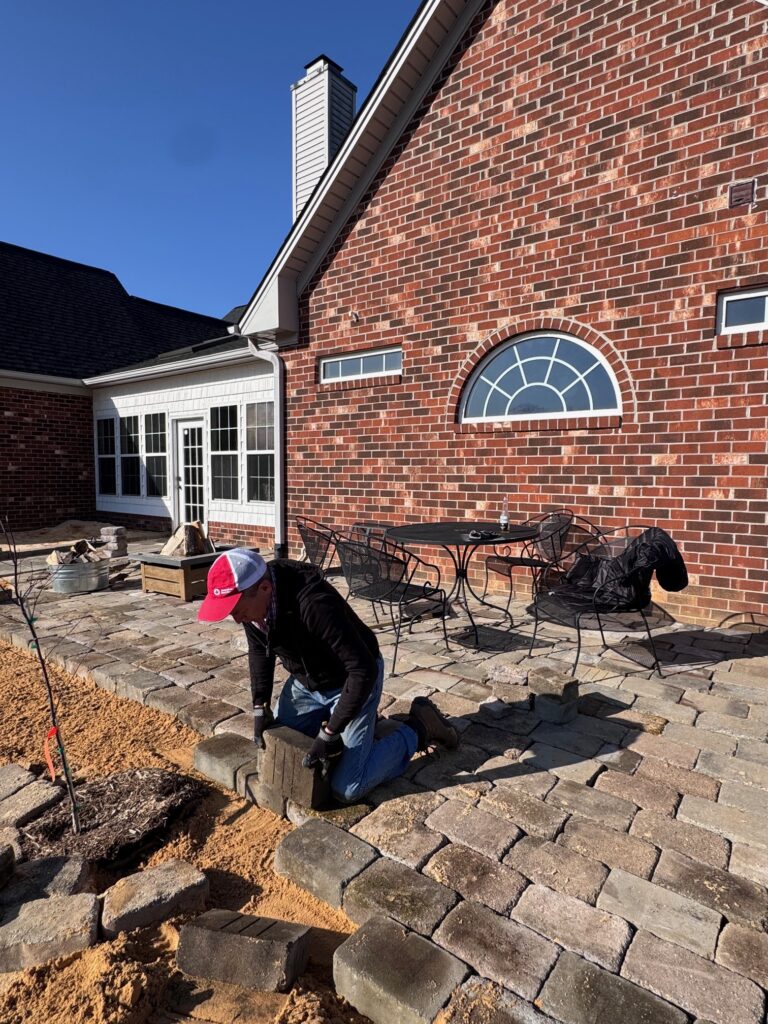 An owner of Willow and Stone Events lays stone pavers for the new back patio at The Retreat, creating a tranquil space for guests.